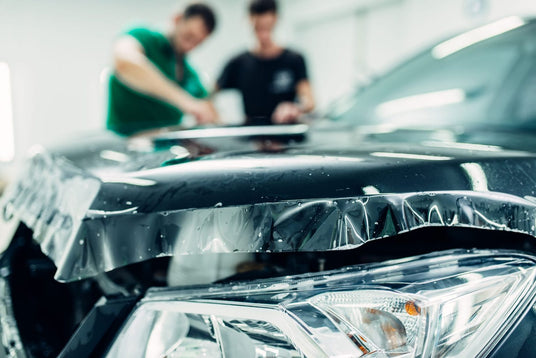 vehicle hood with paint protection film,  two men working on a car